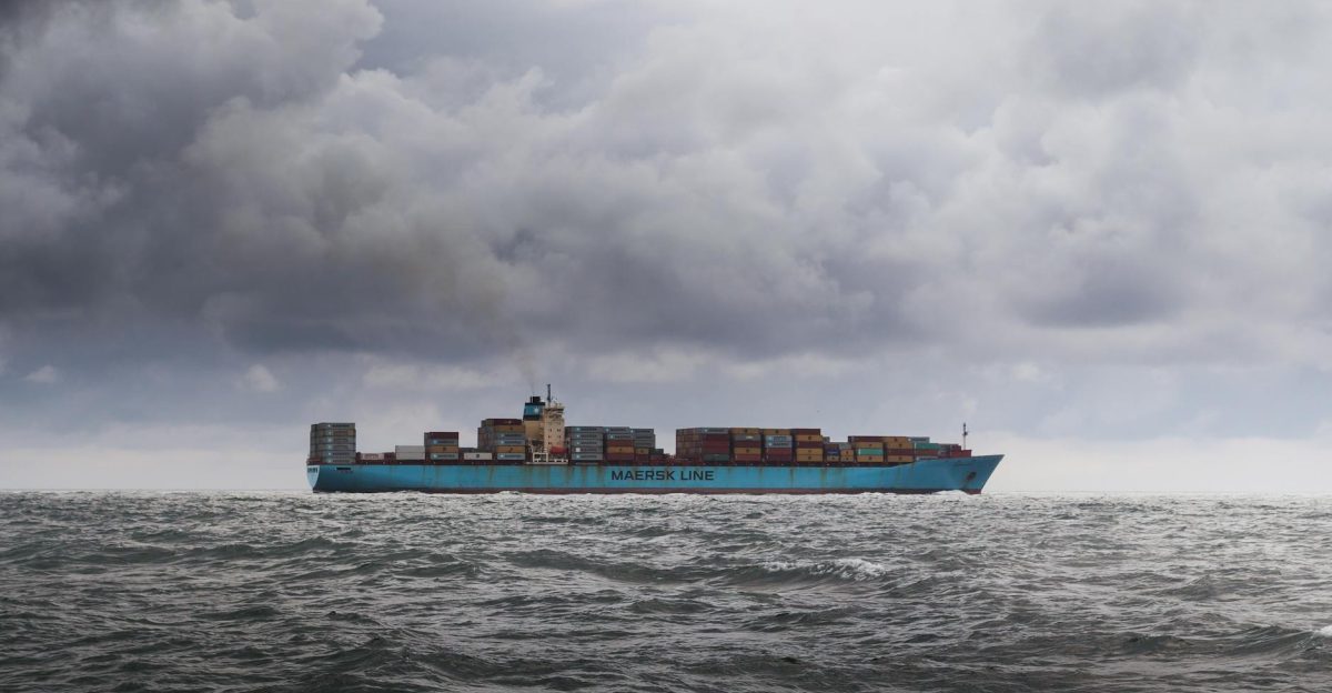 A large cargo ship carrying containers on a cloudy ocean horizon