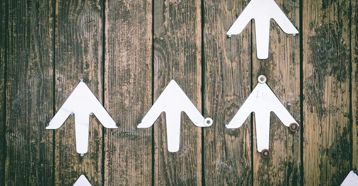 Several white arrows pointing upwards on a wooden wall