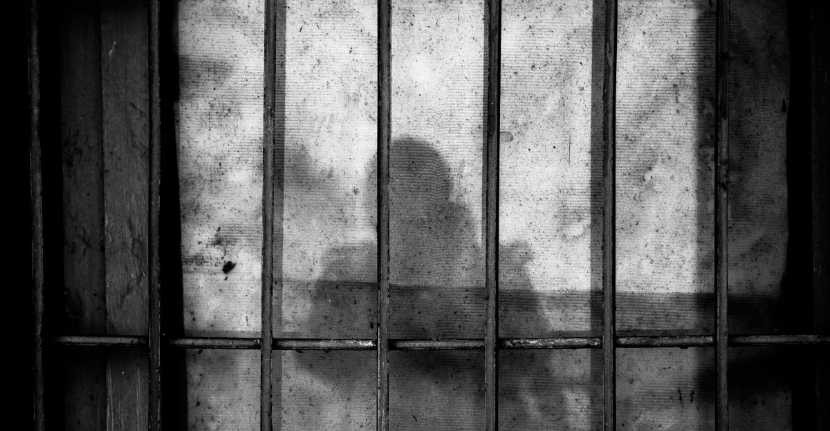 a shadow of a person behind bars in a jail cell