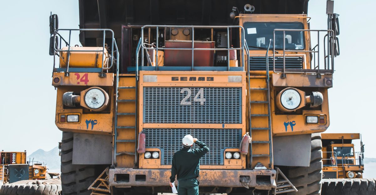 man in brown jacket standing beside yellow truck
