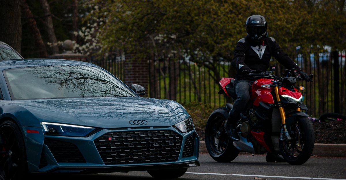 a man riding a motorcycle next to a blue sports car