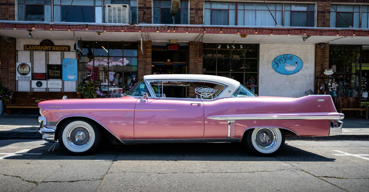 A pink classic car parks in front of a store