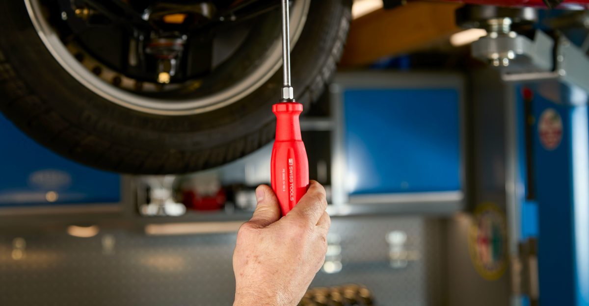Mechanic s hand using screwdriver on car underside
