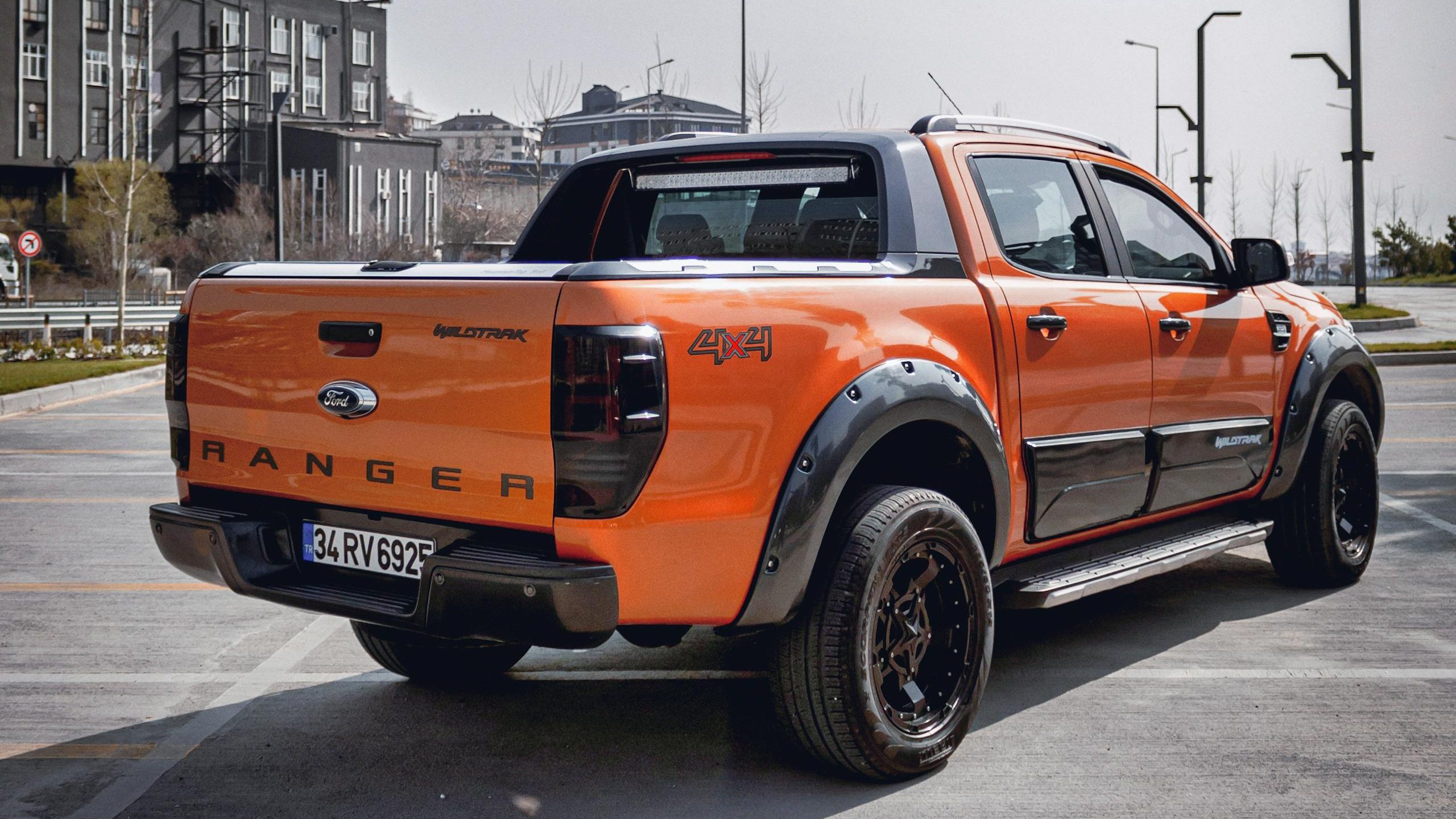 Vibrant orange Ford Ranger pickup truck parked in a modern urban setting under clear skies.
