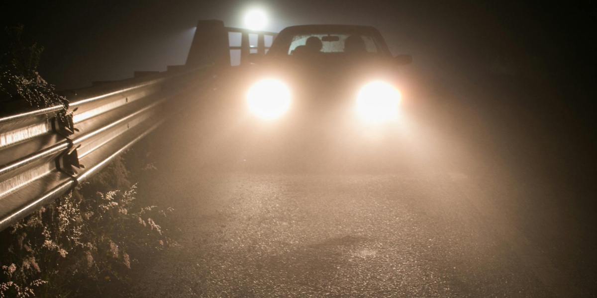 A mysterious car driving at night through foggy Coatepec, headlights illuminating the road.