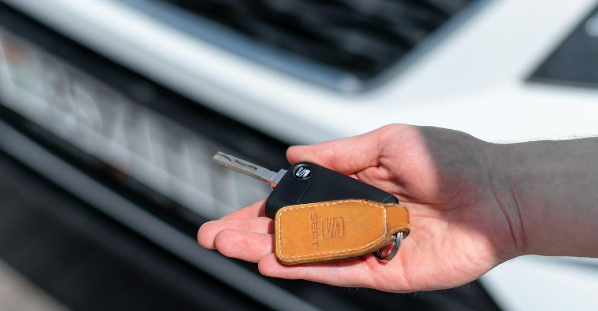 Close-up of a hand holding a car key in front of a white vehicle Ideal for automotive themes