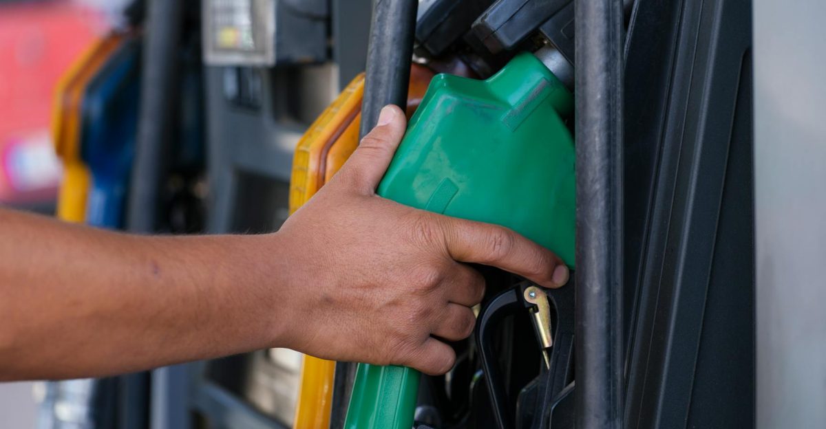 Close-up of a hand holding a green fuel nozzle at a gas pump station outdoors