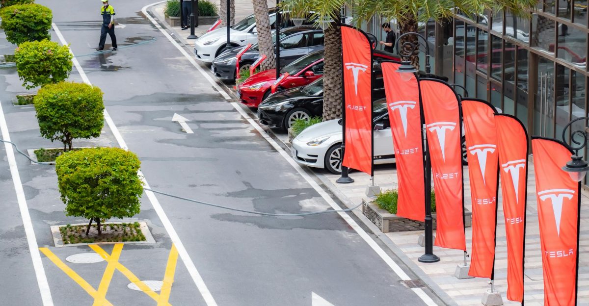 Aerial view of multiple Tesla cars parked alongside branded flags in a city street