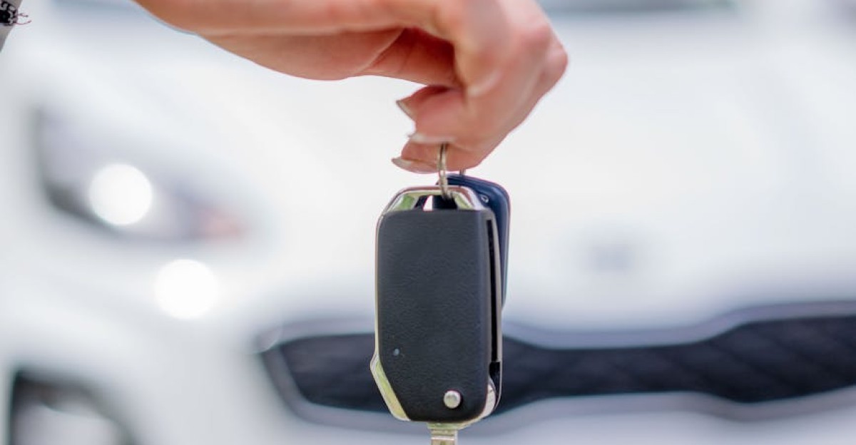 Close-up of a hand holding a car key with a white car in the background outdoors