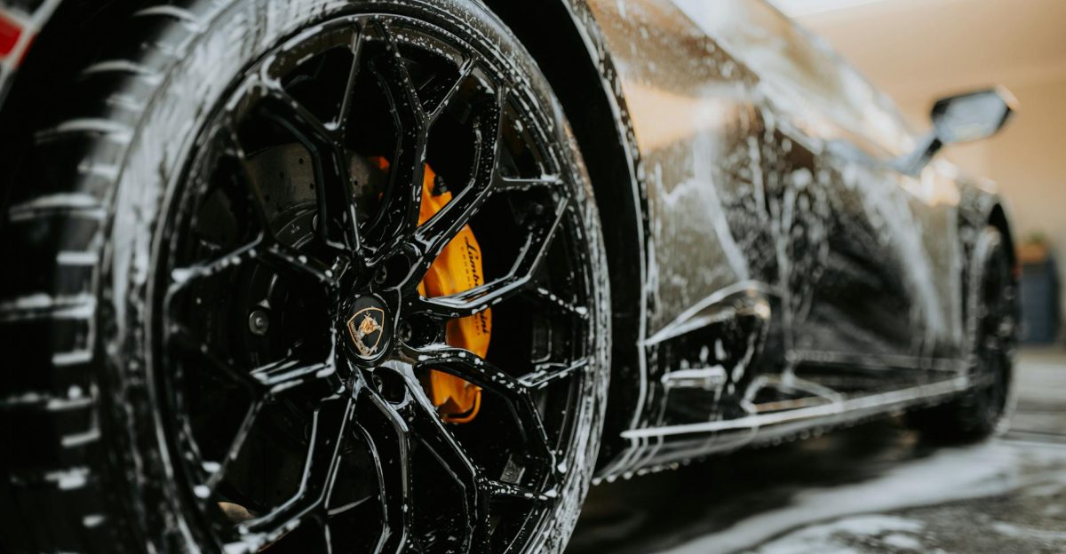 Detailed close-up of a luxury car wheel covered in soap suds during a professional car wash