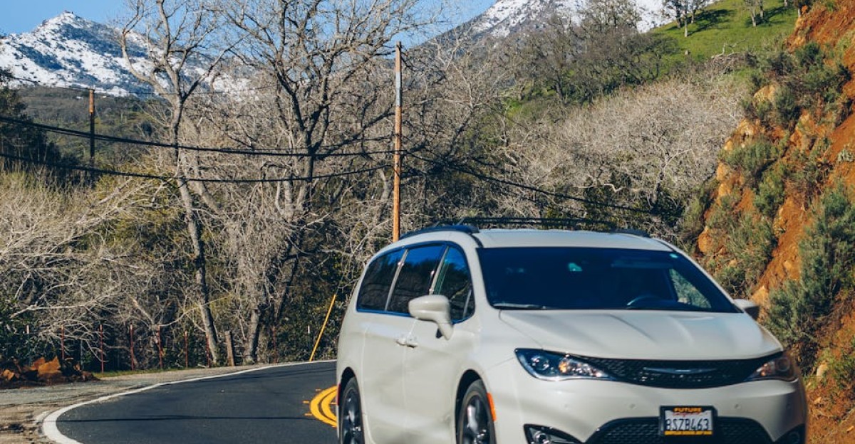 Minivan driving along a winding mountain road with snowcapped peaks