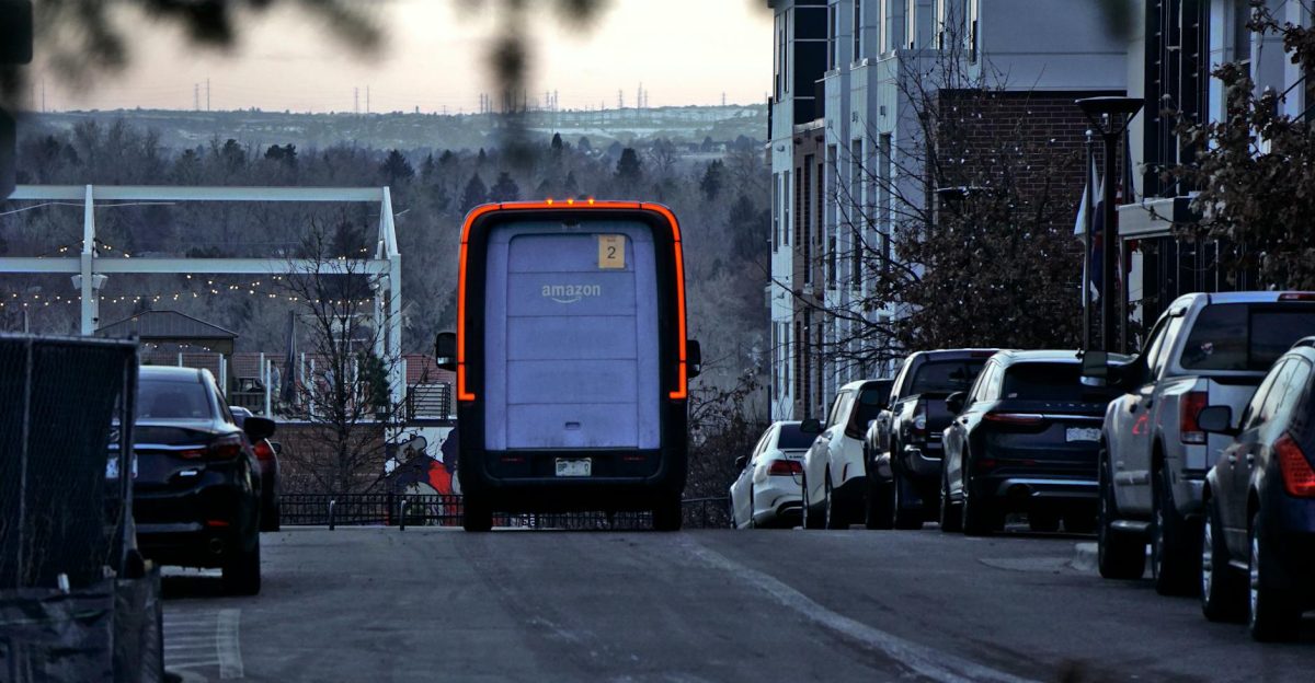 Amazon delivery van driving through an urban street at twilight with cars parked along the side