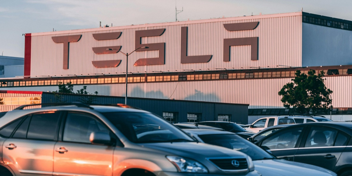 Tesla factory with parked cars during sunset, showcasing modern automotive industry vibes.
