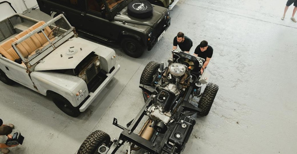 A bustling auto workshop with mechanics restoring vintage Land Rovers viewed from above