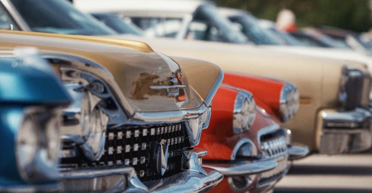 Colorful vintage cars lined up in perfect alignment at an outdoor car show under a clear sky