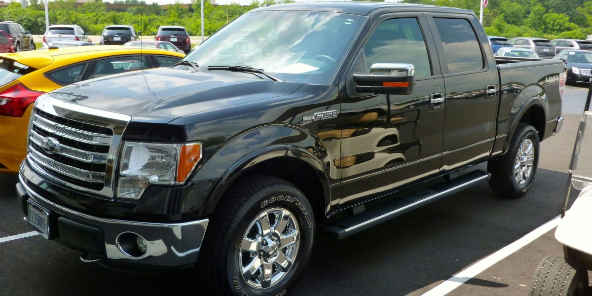 Black Ford F-150 pickup truck displayed at an outdoor dealership lot on a sunny day.