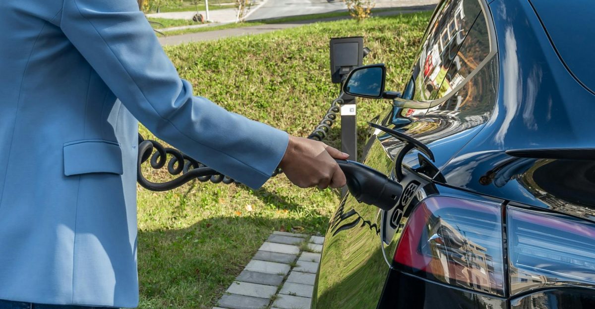 Person connecting an electric car to a charging station outdoors showcasing green energy transition