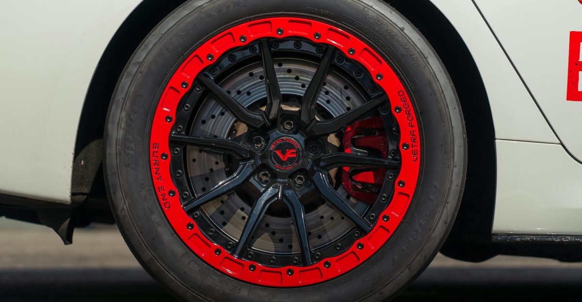 Detailed view of a stylish car wheel featuring a vibrant red and black rim on a white vehicle