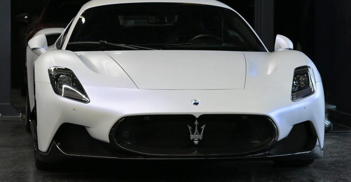 Front view of a striking white Maserati supercar showcased in a dimly lit garage setting