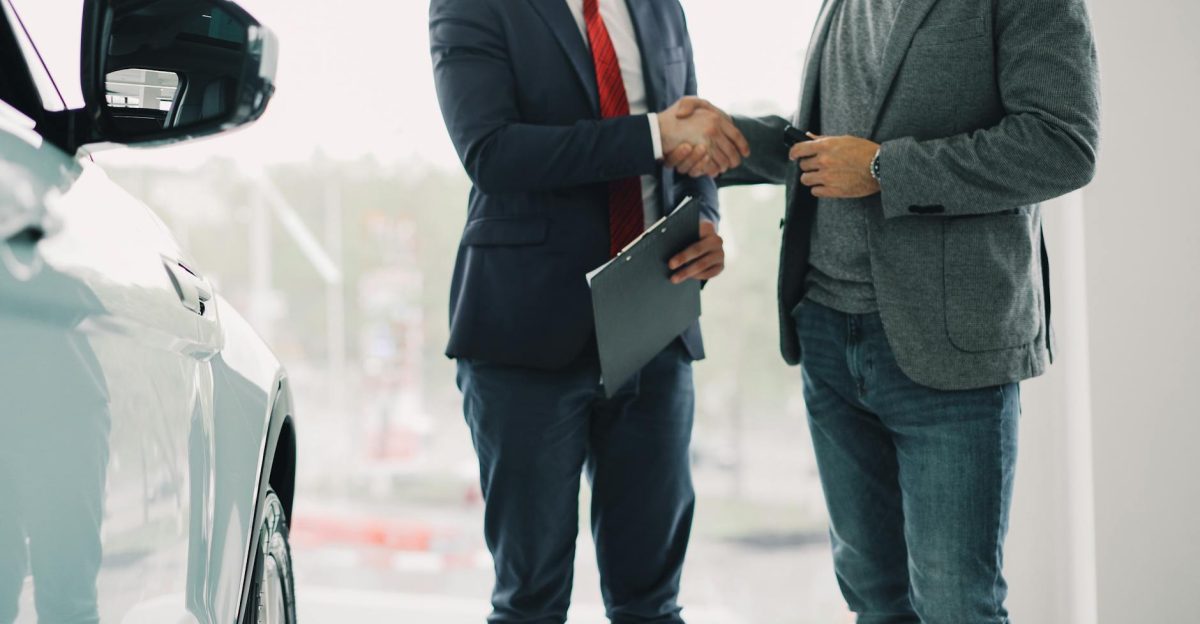 Two men shake hands in a car dealership sealing a business deal