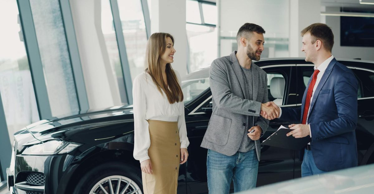 Customers shaking hands with dealer in showroom sealing car purchase deal