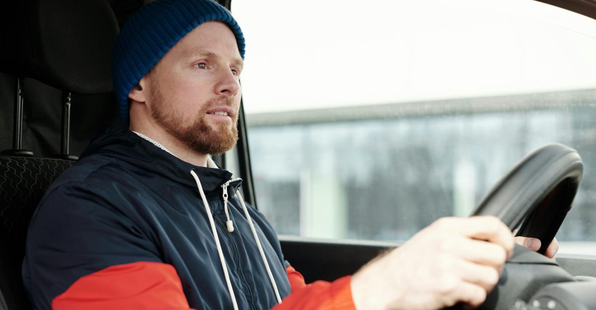 A bearded man wearing a hoodie and knitted cap driving a car focused and attentive