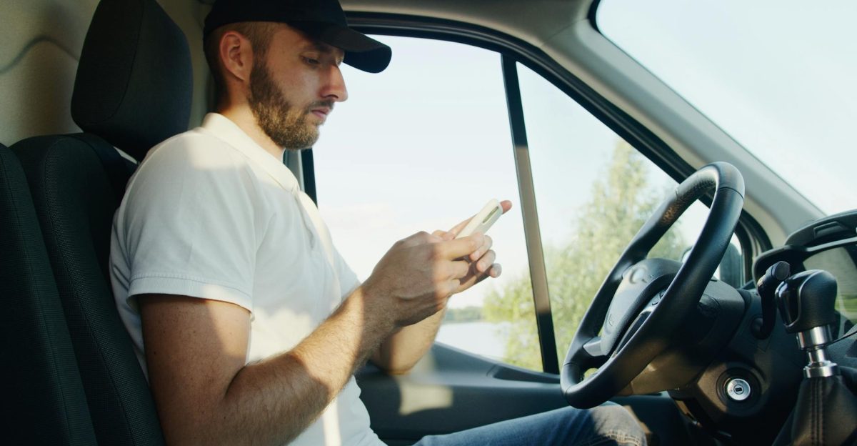 Side view of a man using a smartphone in a parked vehicle on a sunny day