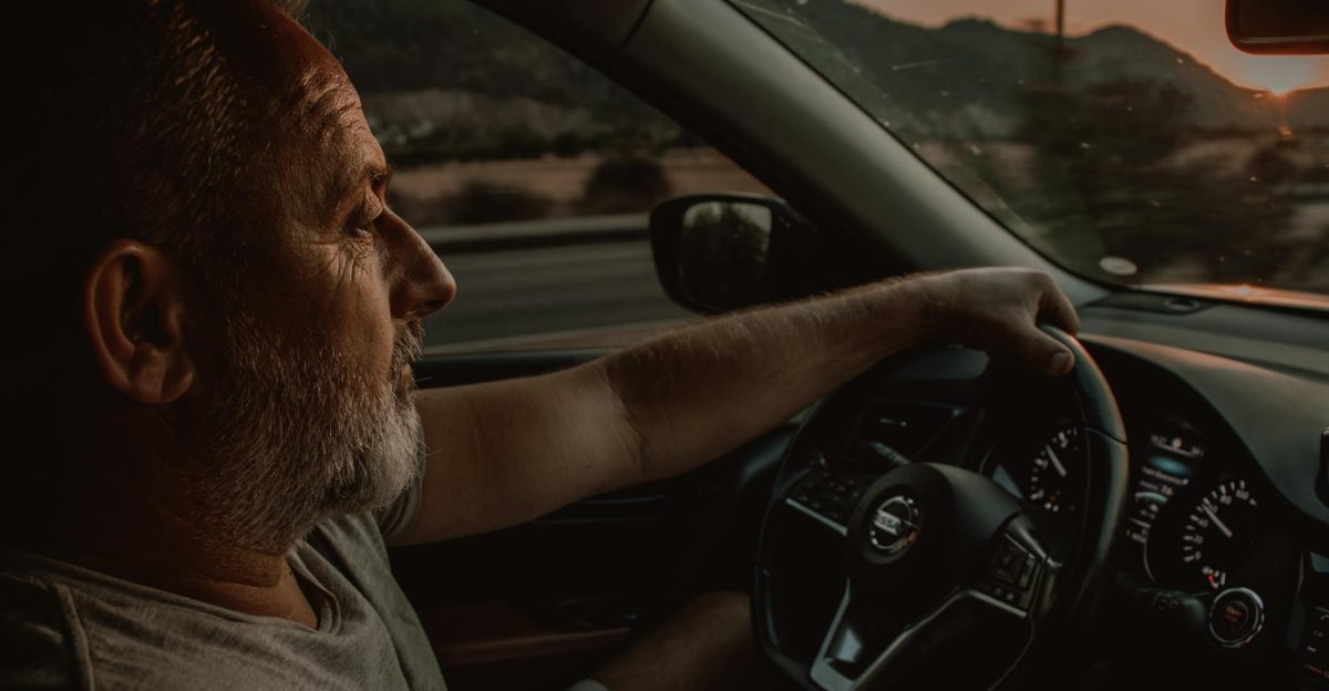 Elderly man driving a Nissan car during sunset depicting travel and contemplation