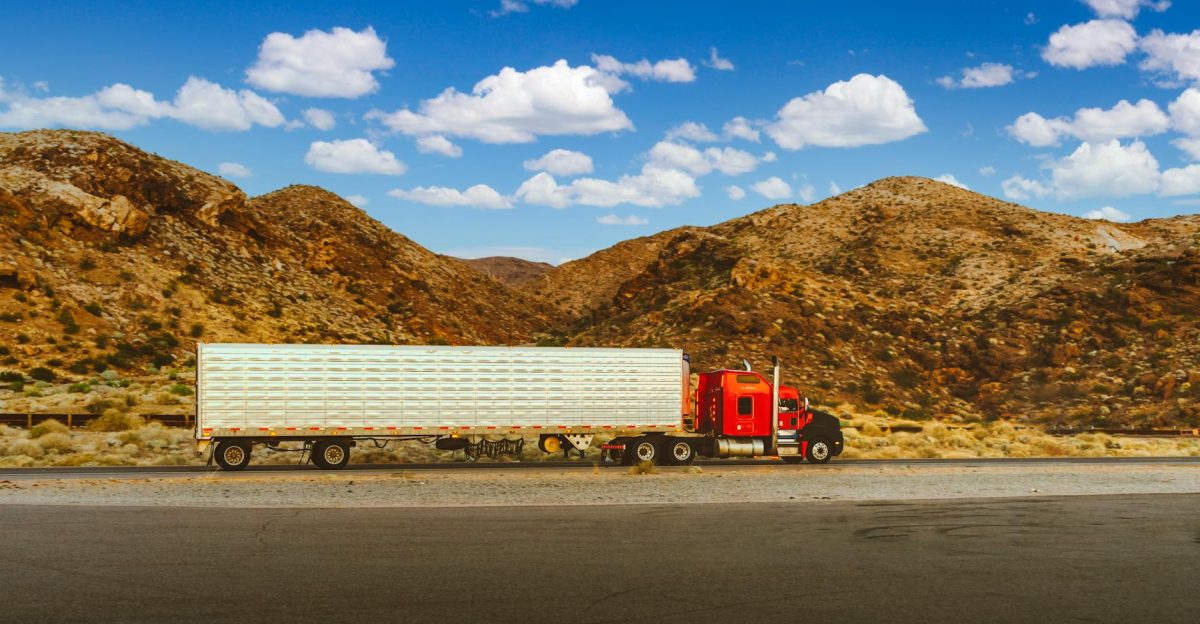 A vibrant red semi-truck travels through a desert highway with mountain views in Nevada