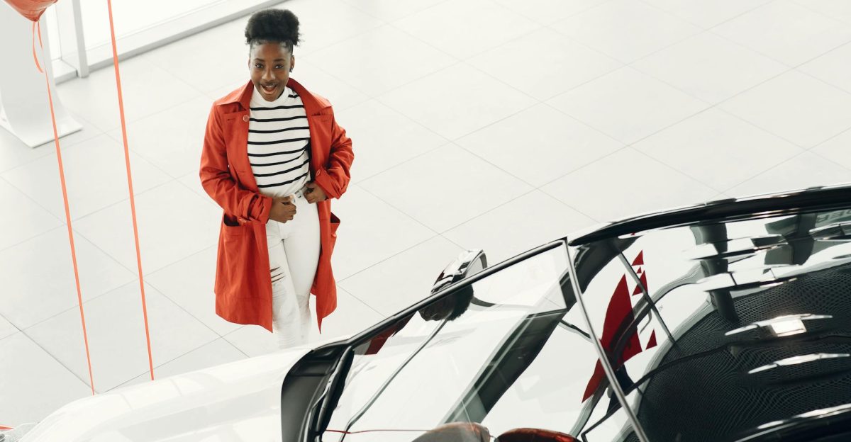 Cheerful woman in red coat exploring a new car at a dealership Excited car shopping experience