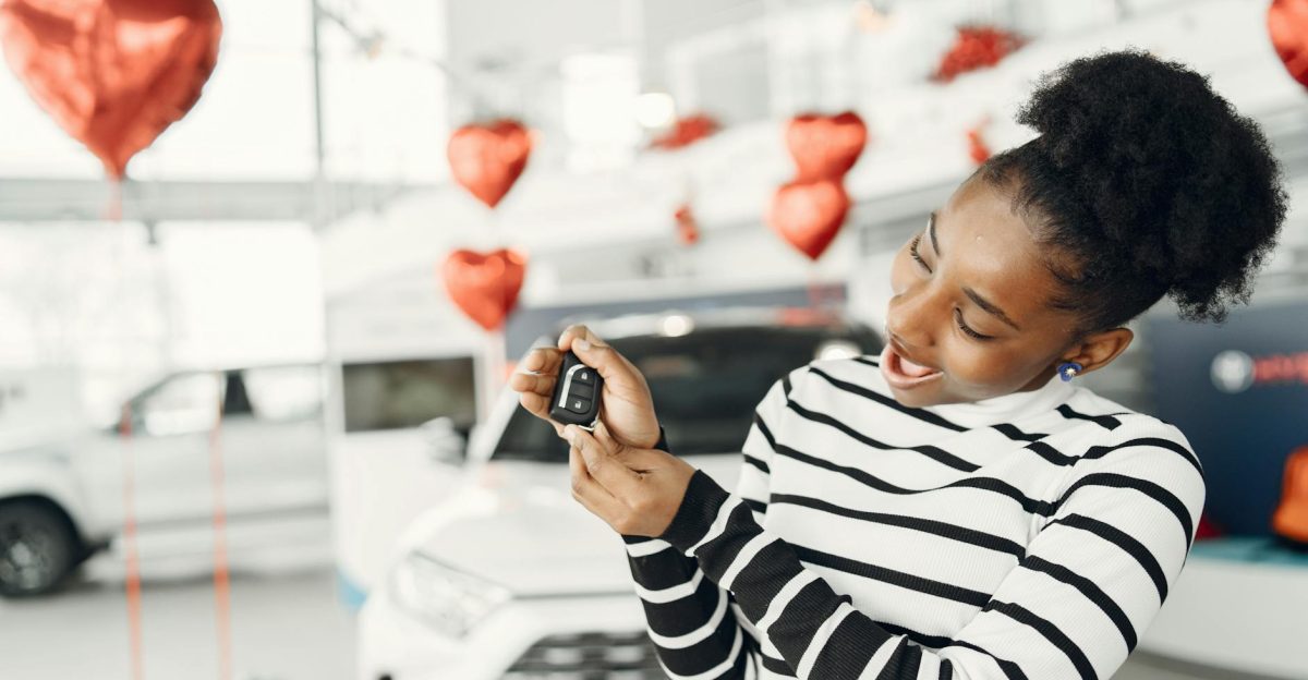 Joyful woman holding car key amidst heart decorations in a showroom