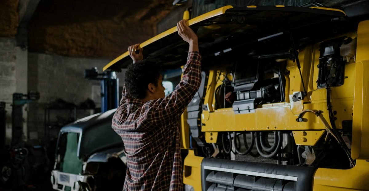A mechanic inspecting a truck engine in a garage setting wearing plaid shirt