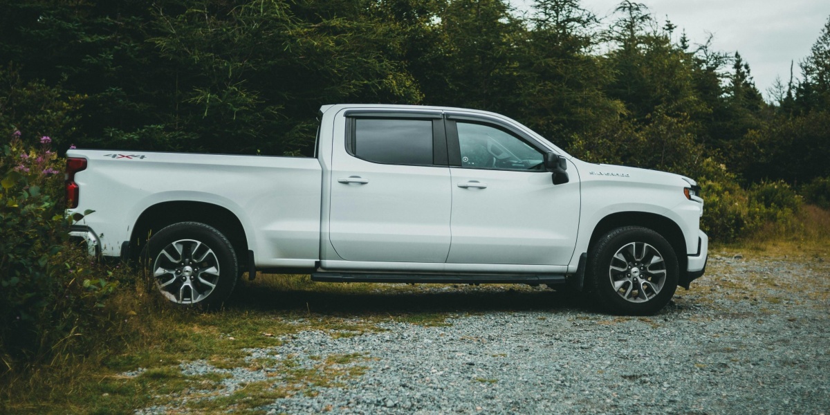 A white pickup truck parked on a gravel path surrounded by green trees in a serene forest setting.