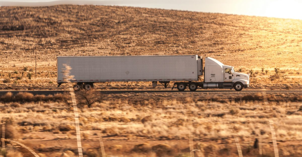 a white semi truck driving down a rural road